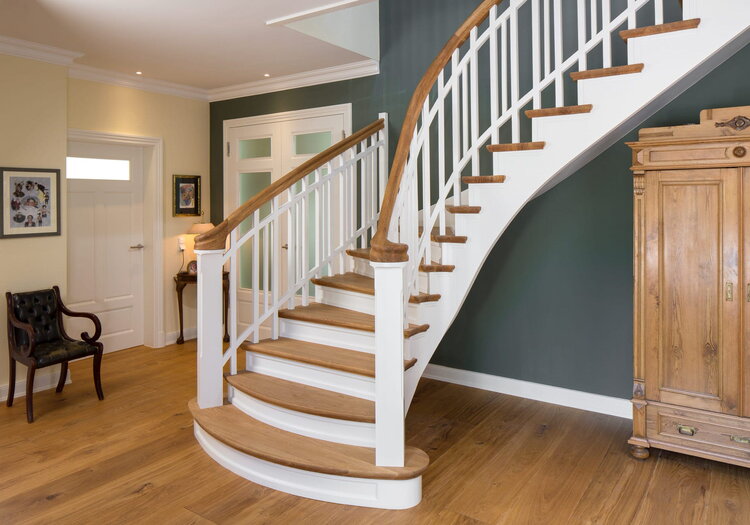 Wandseitig eingestemmte, freiseitig aufgesattelte, geschlossene Wangentreppe. Stufen und Handlauf in der Holzart Eiche geölt. Treppe am Antritt mit zwei Schneckenpfosten trompetenförmig geöffnet. Krümmlinge im Handlauf und den Wangen.