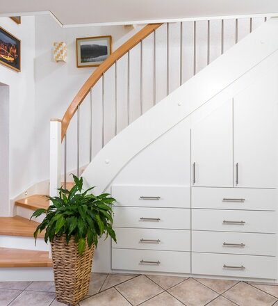 Beidseitig eingestemmte, geschlossene Wangentreppe mit Unterbauschrank und Stellwand. Stufen und Handlauf in der Holzart Buche mosaik farblos lackiert, Wangen, Pfosten und Setzstufen weiß endlackiert.