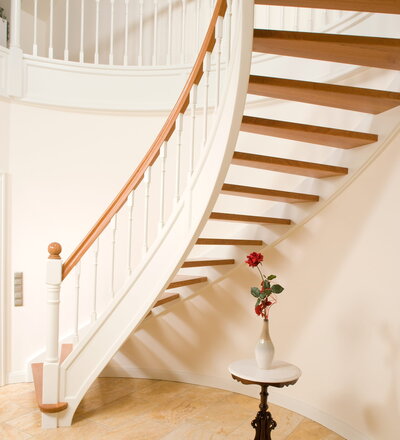 Offene Bogen-Wangentreppe im Landhausstil; Stufen und Handlauf Holzart Kirschbaum; profilierte Wange und Deckenverkleidung