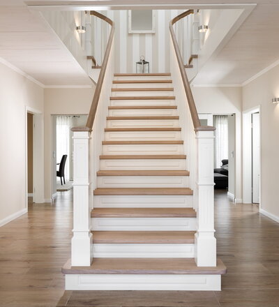 Aufgesattelte, geschlossene Wangentreppe. Stufen und Handlauf in der Holzart Eiche weiß transparent gewachst und geölt, profilierte Setzstufen, LED-Lichtband in den Handlauf eingearbeitet, unterseitiger Abstellraum.