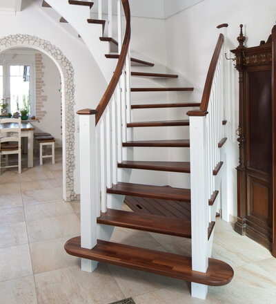 Wandseitig eingestemmt und freiseitig aufgesattelte offene Wangentreppe; Handlauf und Stufen Holzart Akazie mosaik, Wangen, Stäbe und Pfosten Holzart Whitewood weiß endlackiert; Blockstufe am Antritt; Galeriegeländer