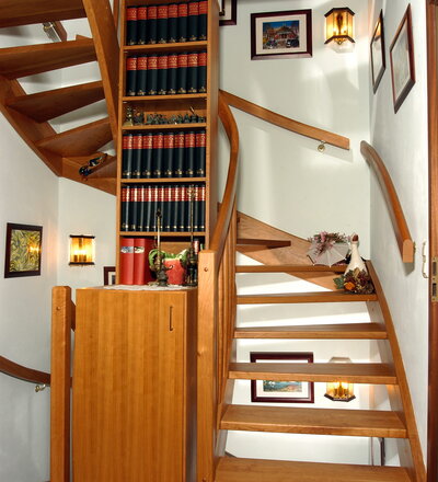 1/2 gewendelte, eingestemmte, offenen Wangentreppe in der Holzart Kirschbaum mit maßgefertigtem Bücherregal im Treppenauge.