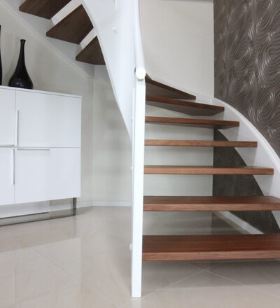 Beidseitig eingestemmte, offene Wangentreppe; Stufen Holzart Nußbaum lackiert; Wangen, Pfosten und Handlauf Holzart Whitewood weiß endlackiert; Brüstungsgeländer und Füllung des Steigegeländers aus ESG-Sicherheitsglas.