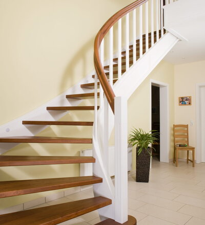 Wangentreppe wandseitig an einen runden Treppenschacht angepasst; freiseitig aufgesattelt mit schwungvollem Innengeländer; Holzart Merbau