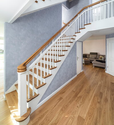 Treppe in Faltwerkoptik. Bauseitige Verkleidung unterhalb der Stufen. Holzart Eiche weiß geölt. Wandhandlauf auf bauseitige Unterkonstruktion aufgeschoben mit Beleuchtung. Statt Brüstung wurde ein Sideboard aufgebaut. (Architektin: Jutta Petersen-Glombek, Hamburg)