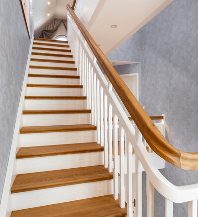 Geschlossene Wangentreppe - Trittstufen, Pfostenköpfe und Handläufe in Eiche klassik farblos geölt. Setzstufen, Wangen, Geländerstäbe und Pfosten weiß lackiert. Trittstufen mit Stufenvorderkanten, Stirnseite profiliert und Setzstufen mit abgesetzter Zierfuge. Handlauf mit integrierter LED-Beleuchtung.