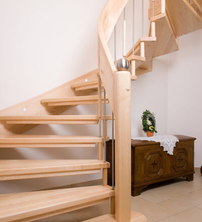 Freitragende Treppe mit wandsetiger Wange und Brüstungsgeländer mit Sicherheitsglas; Stufen am Austrittslauf mit Stäben zur Decke abgehängt; Holzart Europäischer Ahorn.
