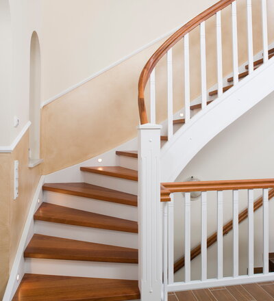 Geschlossene Wangentreppe in der Holzart Merbau mit Krümmling im Wendel, weiße Wangen und Geländer, energiesparende LED Beleuchtung in die Wandwange eingelassen.