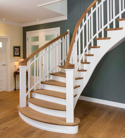 Wandseitig eingestemmte, freiseitig aufgesattelte, geschlossene Wangentreppe. Stufen und Handlauf in der Holzart Eiche geölt. Treppe am Antritt mit zwei Schneckenpfosten trompetenförmig geöffnet. Krümmlinge im Handlauf und den Wangen.