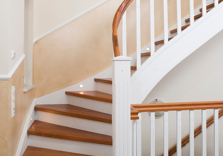Geschlossene Wangentreppe in der Holzart Merbau mit Krümmling im Wendel, weiße Wangen und Geländer, energiesparende LED Beleuchtung in die Wandwange eingelassen.